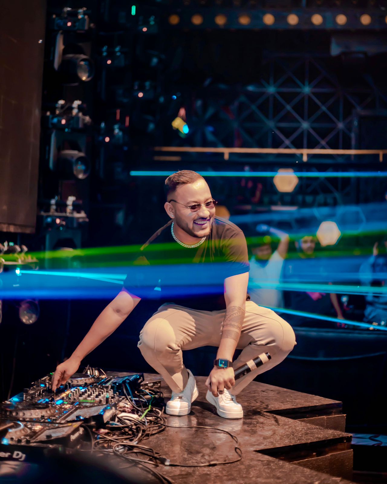 DJ Nihan crouched on stage amid lasers, holding a mic